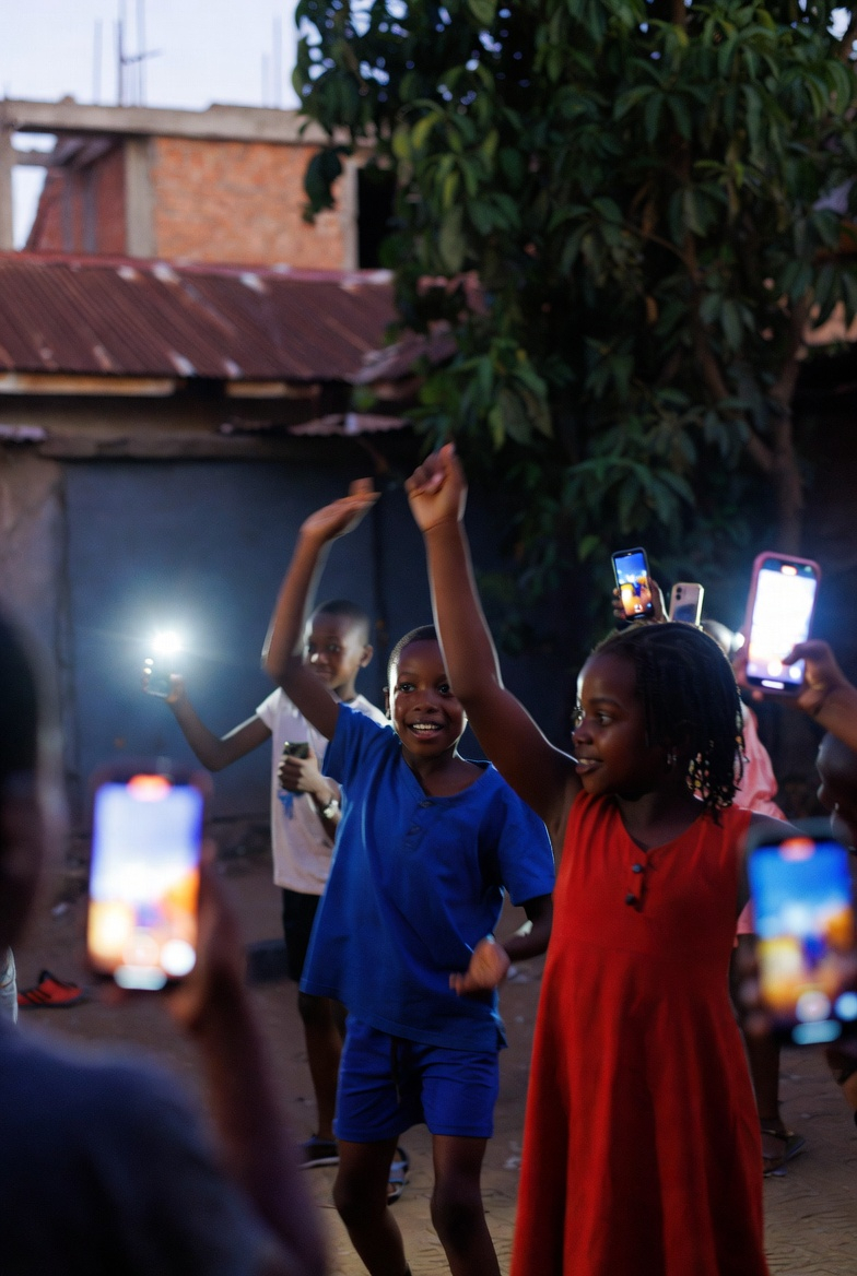 Nairobi kids using phones to record TikTok dances in an estate at dusk, screens glowing, joyful group energy.