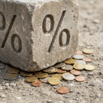 Large stone block with percent symbols crushing a pile of Euro coins on gravel.