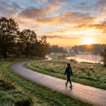 Person walking on curved path beside misty lake at sunrise