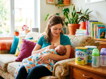 Mother breastfeeding infant wrapped in patterned blanket on couch