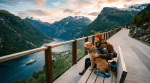 A woman sitting on a bench with her dog overlooking a fjord with mountains and a boat